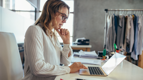 Lady scrolling through her laptop on her desk by a rack of clothes