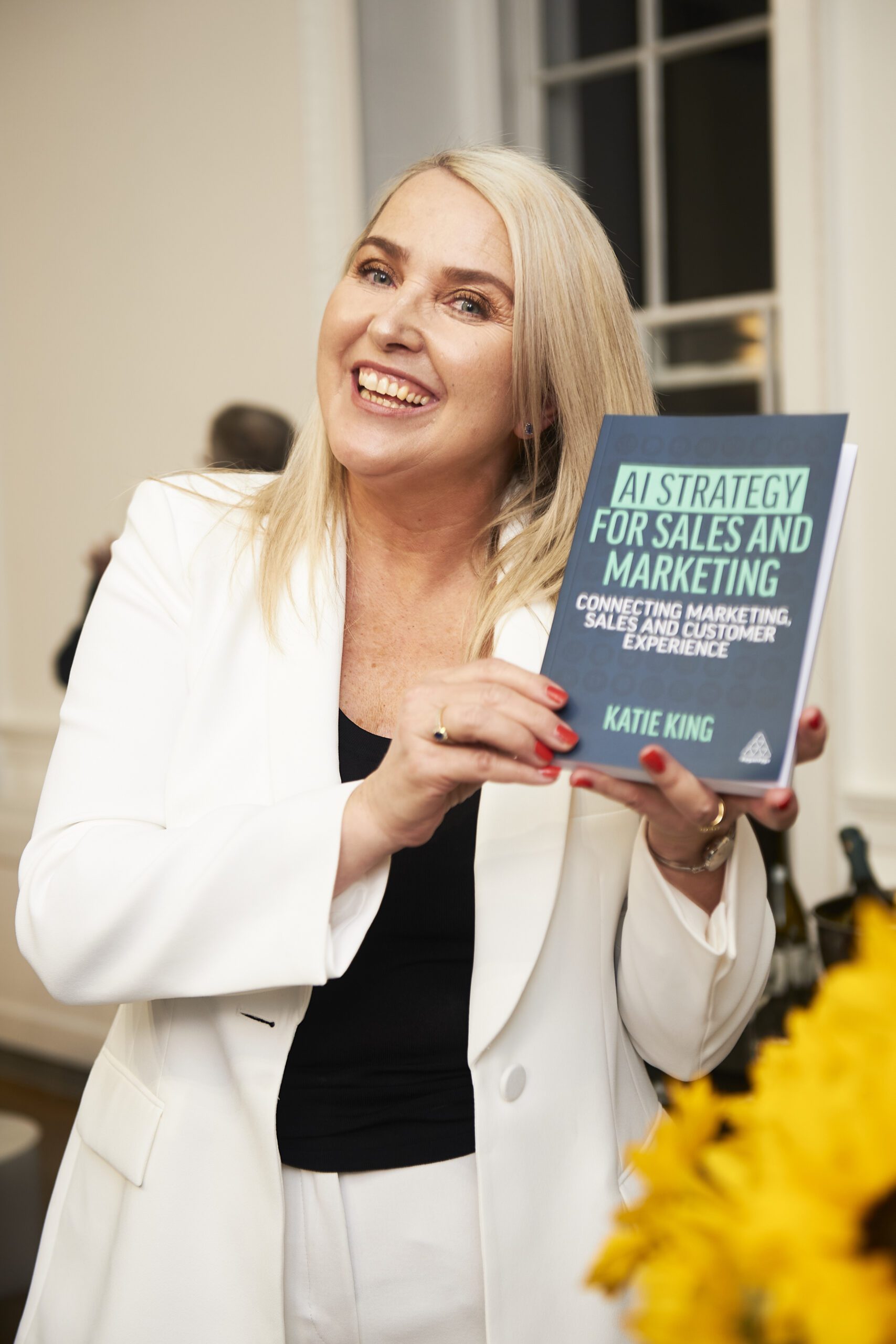 Katie King, speaking at Let's Do Business, holding a book about AI