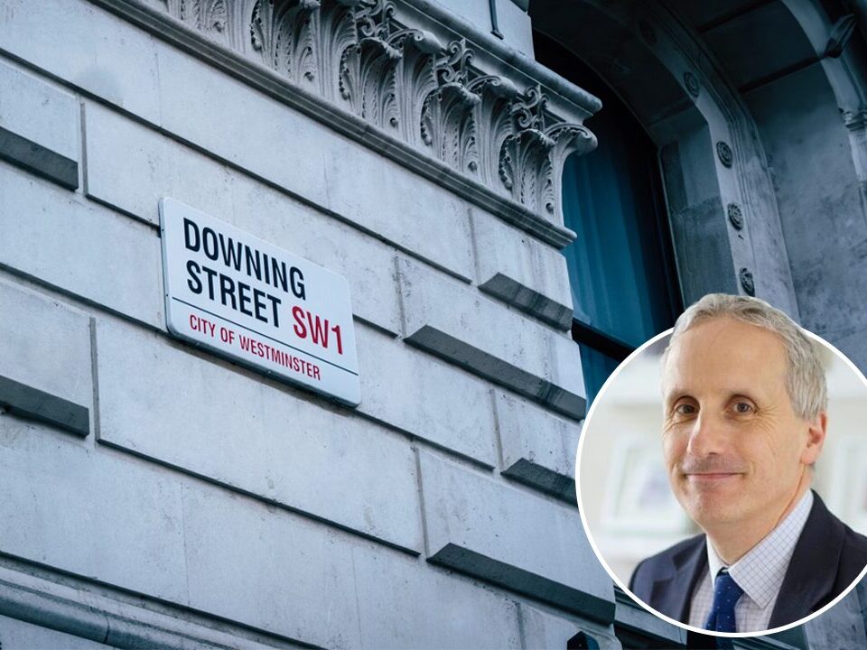 Staffordshire Chambers of Commerce's Declan Riddells headshot in a circle at the bottom right of a picture of Downing Streets road sign on the wall.