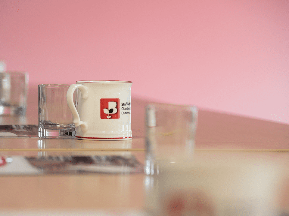 Staffordshire Chambers of Commerce's branded mug on a table with 3 glasses and other collateral in the background.