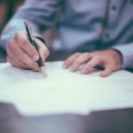 Manin blue suit writing on a piece of paper using his right hand.