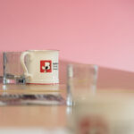 Close-up of a Staffordshire Chambers of Commerce branded mug on a table, with a pink background and glass cups nearby.