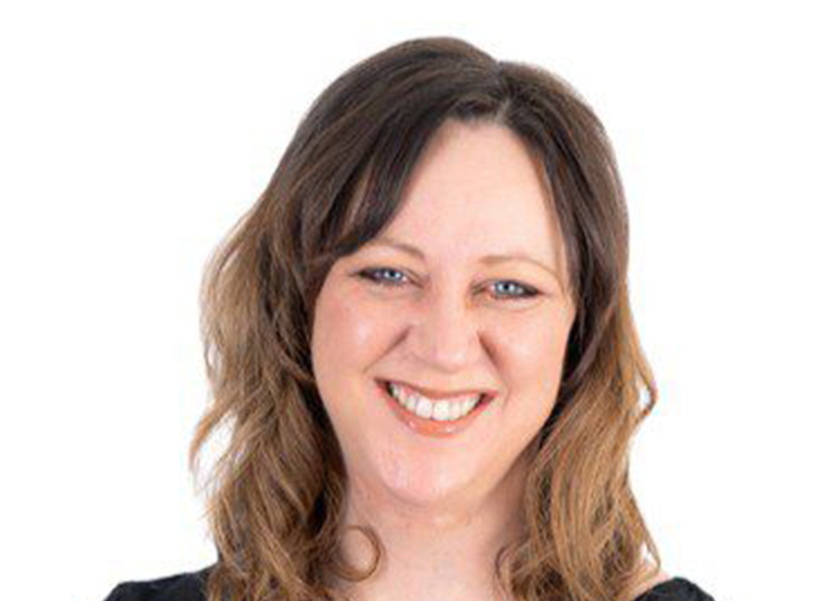 Portrait of Fiona Hawkins, smiling at the camera, with shoulder-length wavy hair, wearing a black top against a white background.