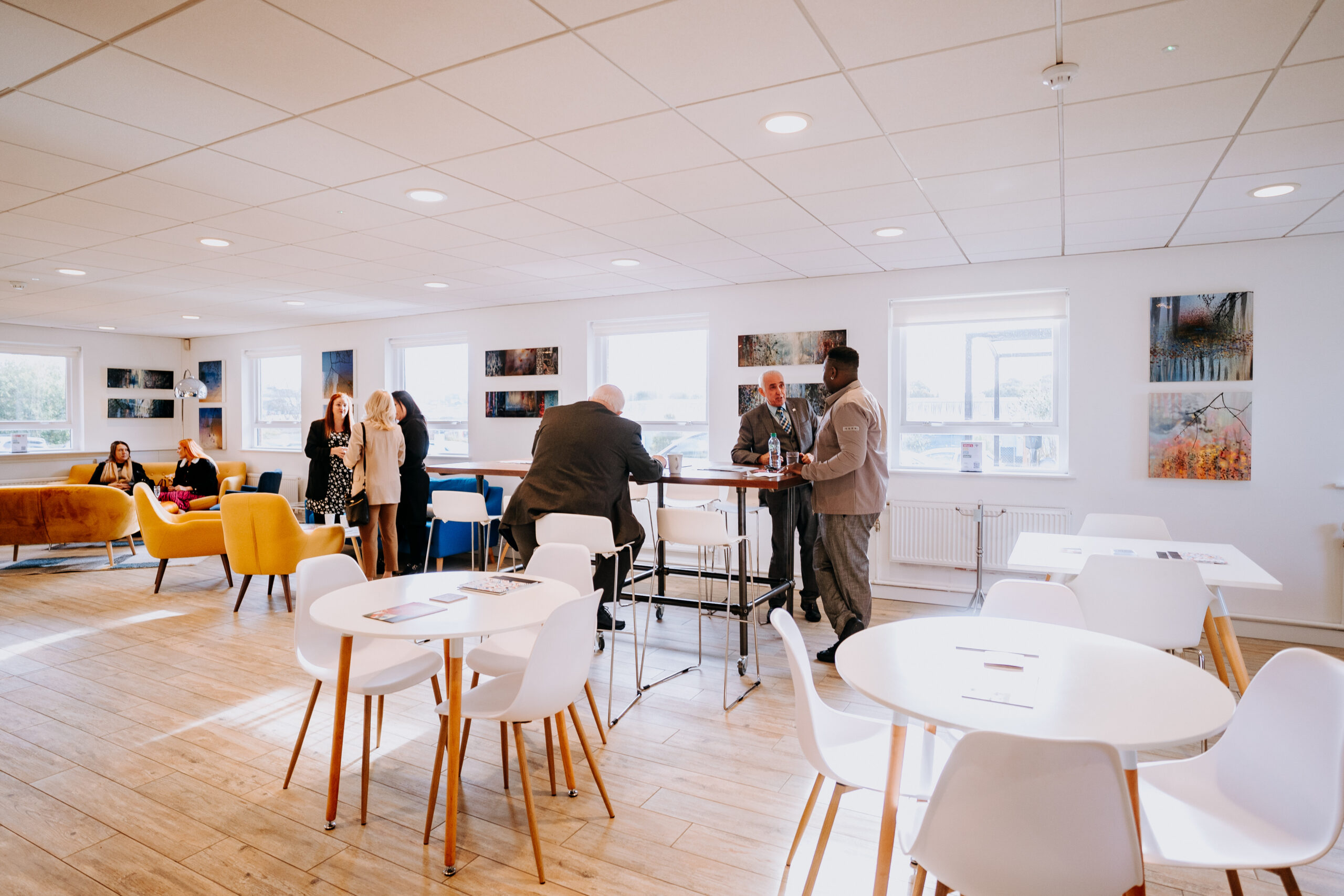 The Staffordshire Chambers Members Lounge, showcasing a bright and inviting space with members engaging in discussions at high tables and relaxing on colorful seating.