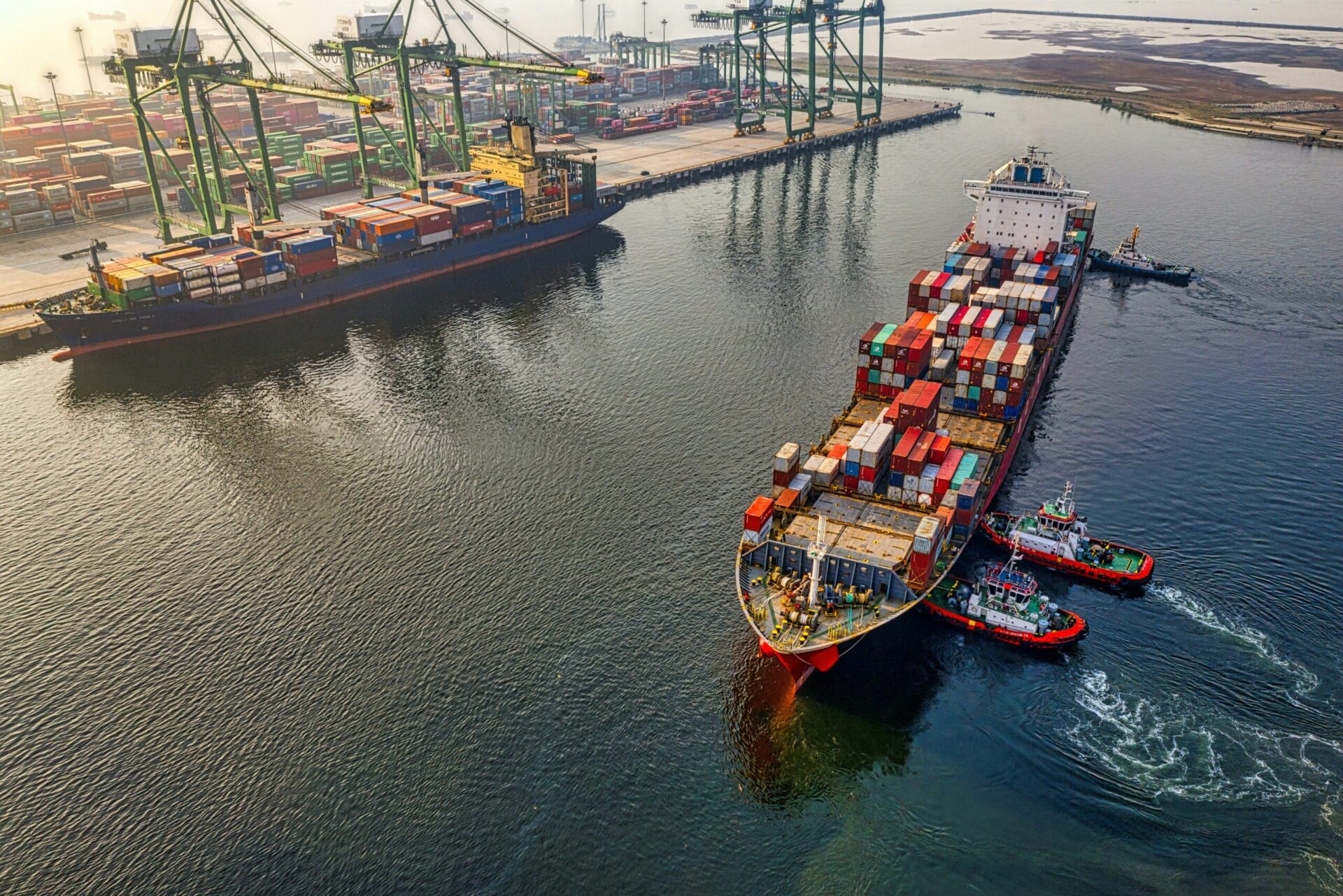 Cargo ships loaded with colorful shipping containers docked at a port with large white cranes and SSA Terminals signage.