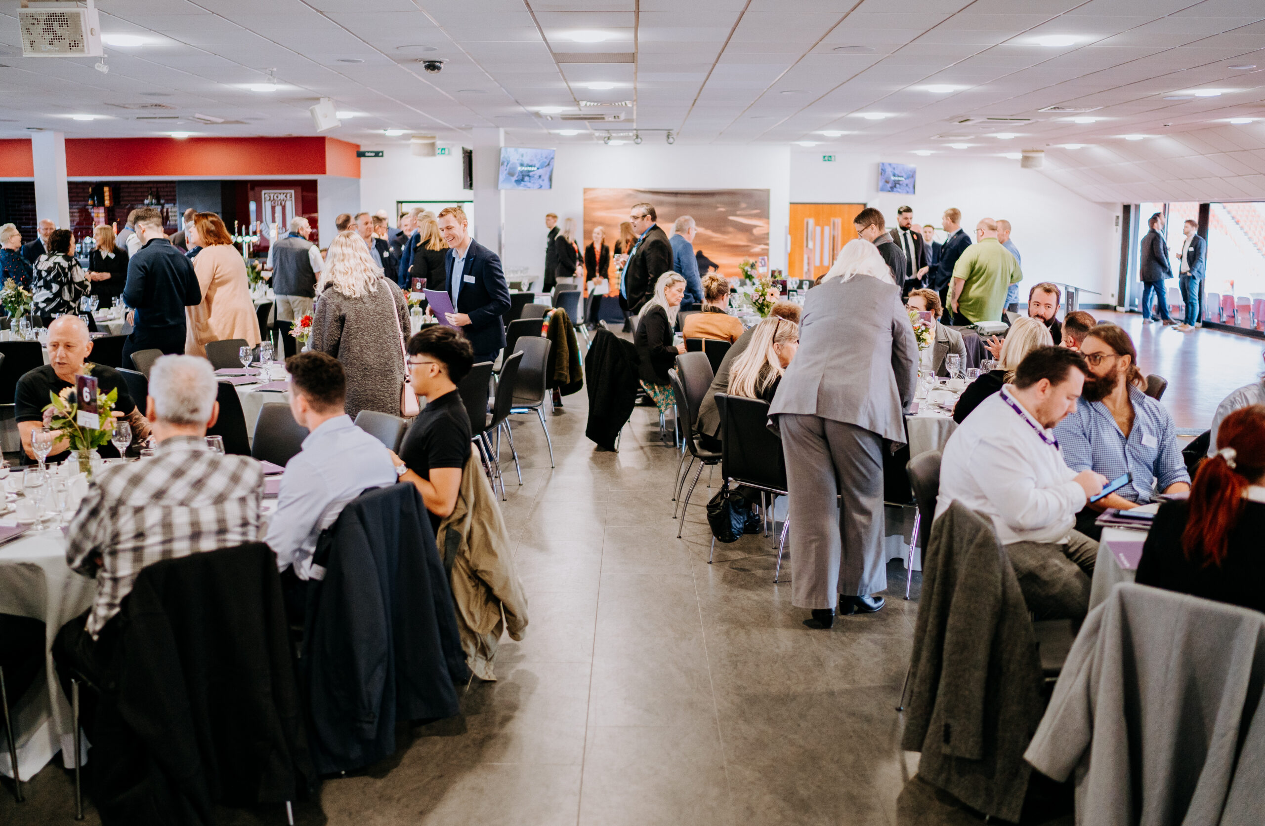 A bustling banquet hall filled with attendees seated at round tables, engaging in conversations during a formal networking event.