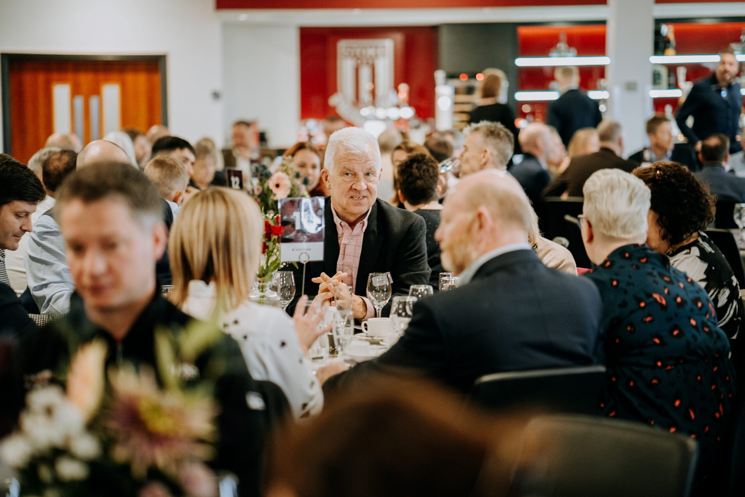 Attendees seated at a formal dining table during a Staffordshire Chambers of Commerce event, engaged in conversation, with a focus on one individual in the foreground.