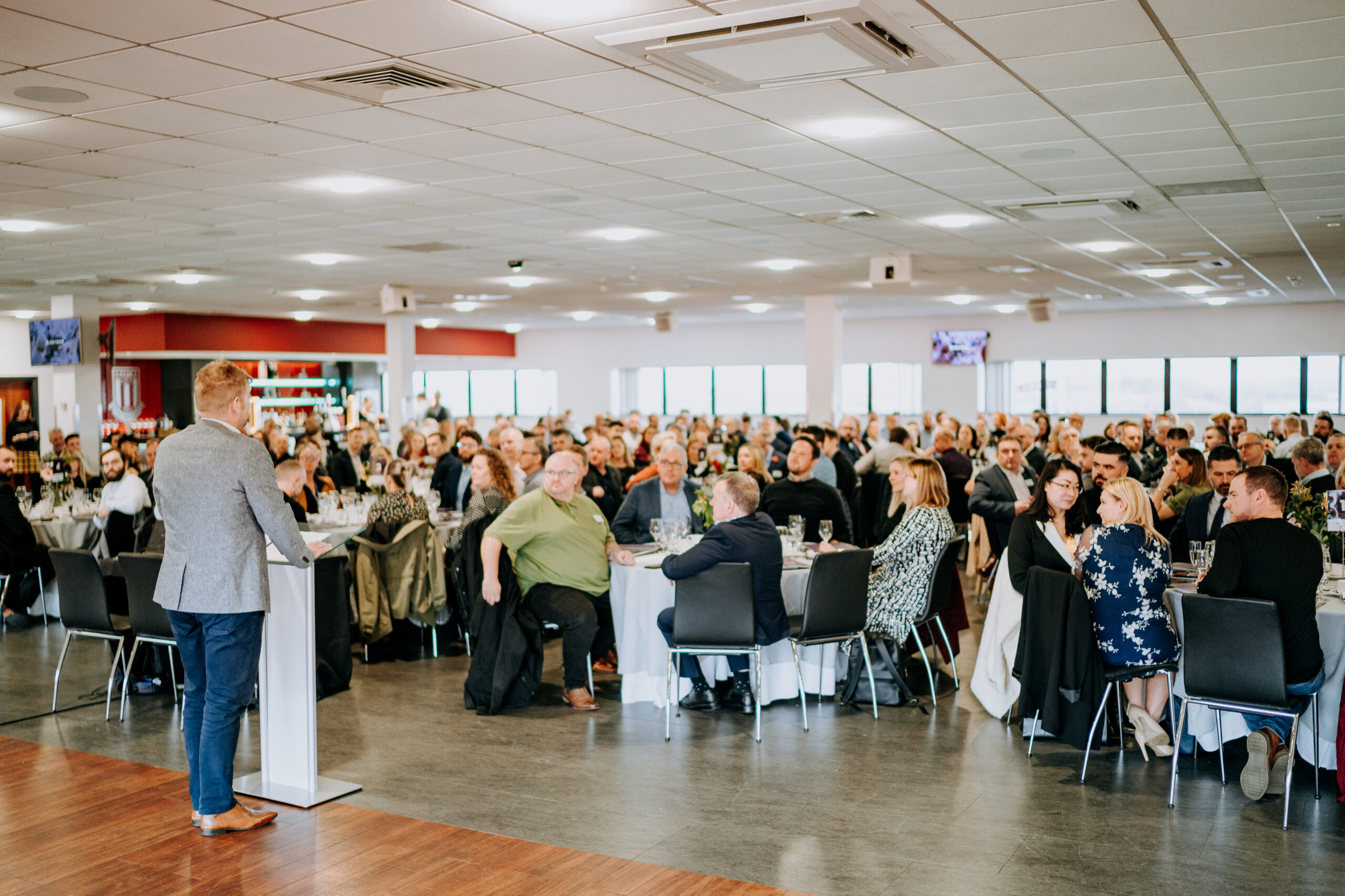 Chris Plant, Deputy CEo at Staffordshire Chambers of Commerce addressing a large audience seated at round tables in a spacious and well-lit banquet hall during a formal event.