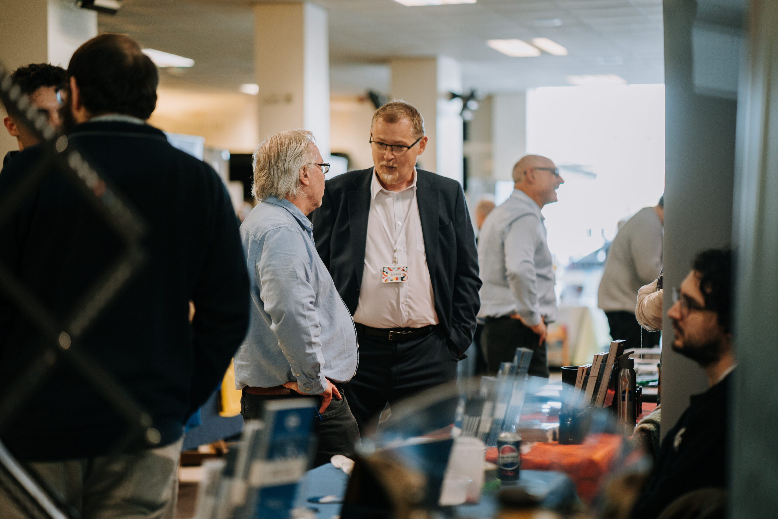 Business professionals engaging in conversation at a networking event hosted by Staffordshire Chambers of Commerce, with informational displays and other attendees in the background.