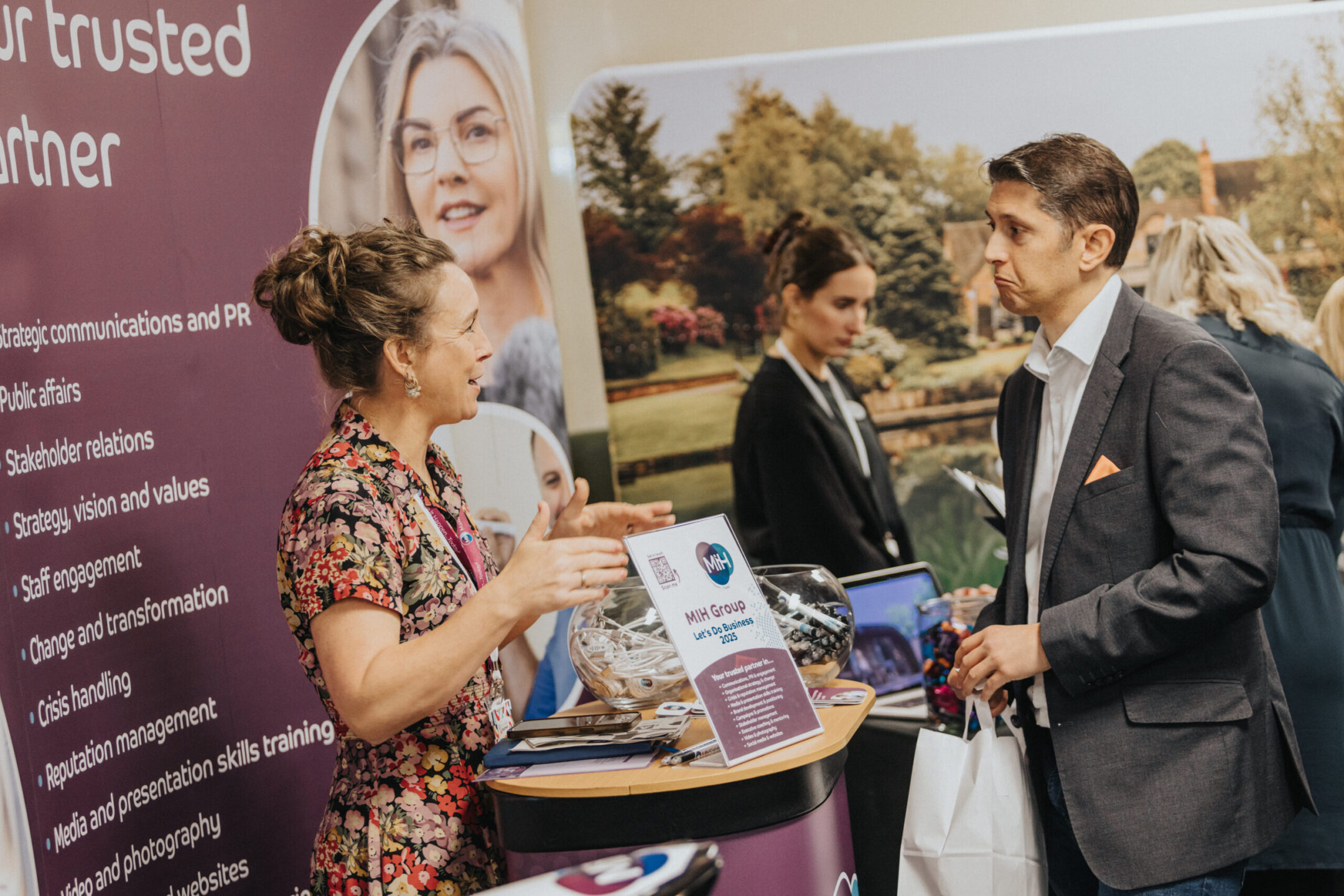 A person at a MIH table at lets do business event 2025 expo talking to staff about MILH Group.
