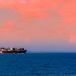Picture of a cargo ship in the middle of the sea at sunset.